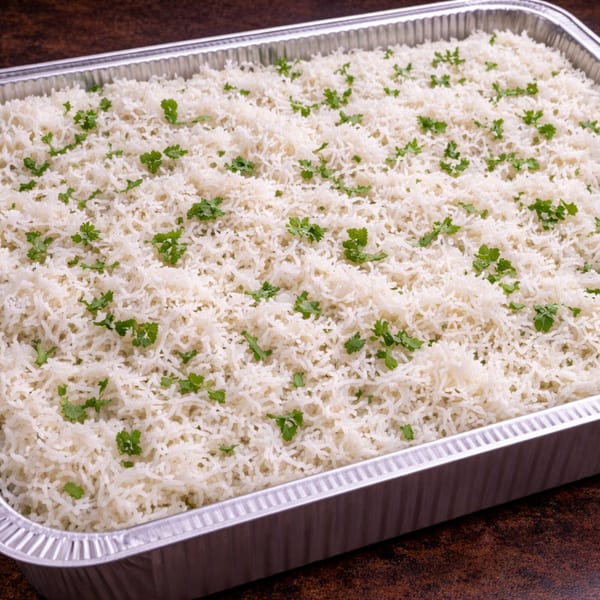 Fluffy white rice with green herb garnish in a large aluminum catering pan.